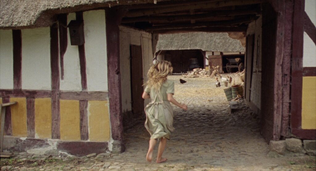 Young girl running through a timber-framed gateway connecting the farm buildings.